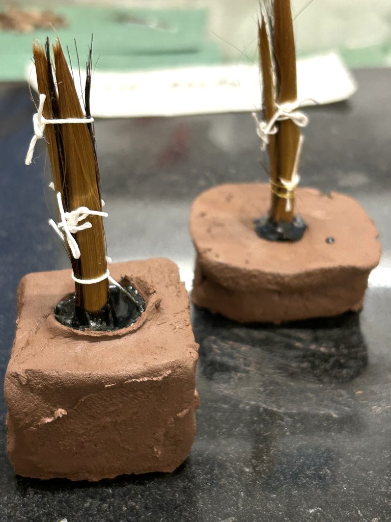 Bristles tied together set in clay. Documentation of making paintbrush.