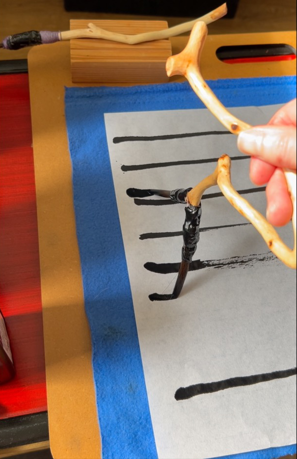 Photograph of a hand holding a paint brush drawing ink lines